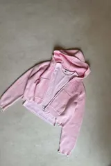 Campera con capucha de tejido texturizado en color rosa claro, de calce relajado. Presenta cierre frontal completo con tirador en forma de aro, bolsillos tipo canguro y logo en relieve del mismo tono en el pecho. Terminaciones con puños y ruedo de borde sin rematar.