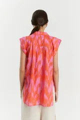 Camisa sin mangas de voile de algodón con estampado abstracto en tonos rosados y anaranjados. Tiene cuello camisero, cartera con botones a la vista, tajos laterales y bolsillo de parche en el delantero.