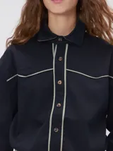 Camisa de estilo western confeccionada en algodón grueso color negro. Presenta detalles de costuras decorativas en tonos claros en el pecho y a lo largo de la cartera de botones. Posee cuello clásico, cierre frontal con botones y un calce holgado.