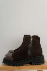 Bota corta de gamuza marrón con puntera de cuero liso, suela track negra y correa desmontable con tachas metálicas.