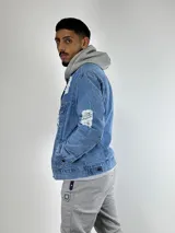Campera de jean celeste con roturas y desgaste, de corte clásico, con cuello camisero, cierre frontal con botones metálicos, bolsillos con solapa abotonada en el pecho y bolsillos laterales.