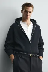 Chaqueta de punto compacto con capucha, confeccionada en hilatura con lana. Presenta cierre frontal con cremallera, mangas largas y acabados en rib.