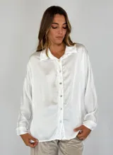 Camisa blanca de satén con cuello clásico, cierre frontal con botones y mangas largas.