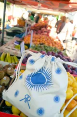 Mochila de tela color crudo con cordones ajustables a tono. Estampado azul con diseño de soles y el isologo de la marca.