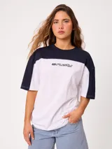 Remera oversize de manga corta marca Rusty, modelo Rocca, en combinación de colores celeste, blanco y detalles en verde. Presenta estampado frontal con el logo de la marca y diseño de bloques de color.