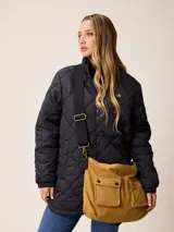 Bolso tipo bandolera de lona color mostaza, con dos bolsillos frontales con solapa y cierre de broche a presión. Cuenta con correas de hombro negras y una correa larga ajustable y extraíble. Presenta herrajes metálicos en tono bronce.