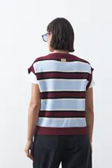 Chaleco tejido de punto con diseño a rayas horizontales en tonos crema, marrón y mostaza. Presenta cuello redondo, cierre frontal con botones y terminaciones acanaladas.