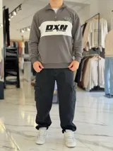 Hoodie de corte clásico con medio cierre y cuello alto, en color marrón con una franja horizontal blanca en el pecho que incluye el logo estampado en negro. Presenta además un pequeño bordado en el hombro izquierdo y puños y cintura elastizados de rib.