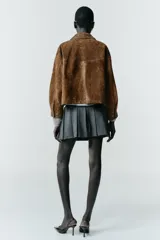 Falda pantalón de tiro alto con diseño de tablas, confeccionada en tejido gris. Incluye un cinturón fino de cuero sintético con hebilla metálica dorada y cierre lateral con cremallera oculta.