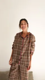 Conjunto de pijama a cuadros con ribetes en color lila, compuesto por camisa de manga larga con botones y pantalón largo.