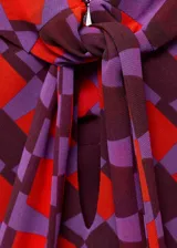 Vestido corto sin mangas con cuello alto, confeccionado en tejido estampado con patrón geométrico en tonos rojos y violetas.