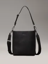 Cartera tipo saco pequeña Calvin Klein color negro, de cuero sintético granulado. Tiene dos correas desmontables: una correa fina ajustable y una correa ancha ajustable con logo jacquard.
