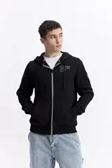 Campera con capucha y cierre frontal, color crema, con bolsillo canguro. Presenta un estampado de texto en el pecho y detalles en el puño.