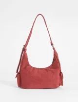 Cartera de hombro color rojo, confeccionada en símil gamuza, con diseño de múltiples bolsillos externos, incluyendo uno frontal con cierre y dos laterales. Cuenta con correa ajustable y logo metálico de la marca en el frente.