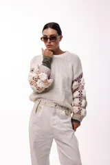 Sweater de punto con cuerpo liso en color negro y mangas largas tejidas en crochet gris con aplicaciones de flores en relieve color blanco.