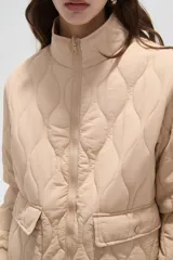 Campera acolchada de poliamida en color beige, con diseño de costuras en rombos, cuello alto, cierre frontal y bolsillos delanteros con solapa.