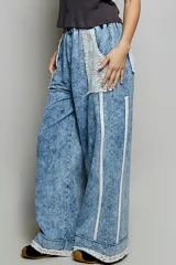 Pantalon de denim azul con lavado vintage, corte ancho y recto, cintura elastizada, grandes bolsillos delanteros de encaje y detalles de ribetes trenzados.