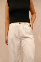 Pantalón de vestir color crudo con rayas diplomáticas negras, de tiro alto, corte sastrero y piernas anchas. Cuenta con bolsillos laterales y cierre frontal con botón carey.