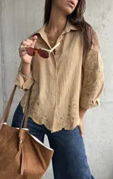 Camisa de lino color camel con cuello clásico, cierre frontal de botones y mangas largas. Presenta un delicado bordado floral tono sobre tono en las mangas y en el ruedo, el cual tiene un acabado festoneado.