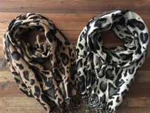 Bufanda con estampado animal print, una en tonos beige y negro y otra en blanco y negro, ambas con flecos en los extremos.