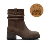Bota de caña media confeccionada en cuero, con diseño de efecto arrugado en la parte superior y detalle de tira con botón a presión. Cuenta con taco cuadrado de altura media y suela track dentada.