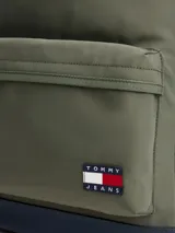 Mochila de diseño redondeado en color verde militar con base en azul marino. Cuenta con un compartimento principal con cierre de cremallera, un bolsillo frontal con cierre, asa superior y correas acolchadas ajustables. Incluye el parche distintivo de Tommy Jeans en la parte frontal.
