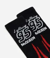 Medias de caña larga con diseño inspirado en Rayo McQueen de Cars. Presentan un estampado de llamas en tonos rojos, naranjas y amarillos sobre una base negra, con el número 95 y el nombre del personaje bordados en la parte superior.