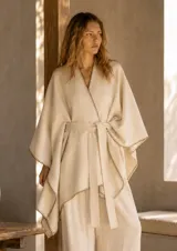 Ruana de corte holgado en color blanco, con diseño tipo kimono, mangas anchas y cinturón ajustable en la cintura. Presenta detalles de costuras decorativas en contraste a lo largo de los bordes.