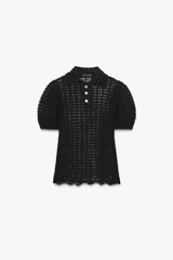 Polo negro de punto calado con cuello clásico, manga corta abullonada y terminación ondulada en el ruedo.