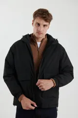 Campera impermeable negra con capucha, cierres a tono y cursores negros metalizados, bolsillos frontales con tapa, elásticos regulables en el ruedo e interior térmico con detalles confeccionados con láser.