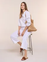 Pantalón crop de lino y algodón color blanco, con calce holgado, pierna ancha de corte recto y cintura elástica. Presenta bolsillos laterales y detalle de puntilla aplicada en el frente.