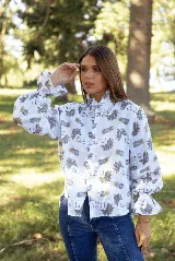 Camisa de lino con estampado floral y tipográfico, cuello alto con volados, cierre frontal con botones y mangas largas abullonadas con puños elásticos.