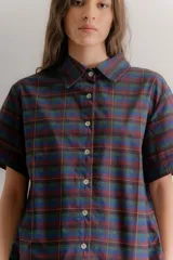 Vestido corto de estilo camisero con estampado de cuadros en tonos azul, verde y bordó. Presenta cuello clásico, cierre frontal con botones y falda tableada con corte a la cadera.