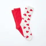 Pack de dos pares de medias de textura suave y afelpada. Un par es de color rojo liso y el otro es de color blanco con estampado de corazones rojos.