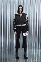 Chaleco biker negro de cuero sintético con forro de borrego beige, cierre frontal metálico, bolsillos laterales con cremallera y cinturón ajustable.