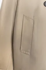 Chaqueta corta estilo trench color marrón oscuro, de corte cruzado con doble botonadura, cuello solapa y hombreras. Presenta mangas largas con puños anchos y bolsillos delanteros de vivo.