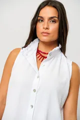 Camisa blanca sin mangas con cuello mao adornado con un delicado volado y cierre frontal con botones.