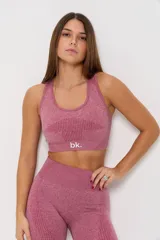 Conjunto deportivo de tres piezas en color rosa viejo, compuesto por un top de bretel ancho, un top de manga larga y una calza chupín. Las prendas presentan un diseño sin costuras con detalles de tejido texturizado y el logo de la marca estampado en blanco.