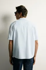 Camisa de manga corta color celeste, de corte regular fit, confeccionada en mezcla de algodón y lino. Presenta cuello camisero clásico y cierre frontal con botones.