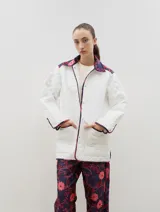 Campera acolchada de corte holgado, color blanco con diseño capitoneado en forma de rombos. Presenta cuello camisero y bordes internos con estampado floral en tonos azul y rojo, cierre frontal con botones a presión y bolsillos laterales.