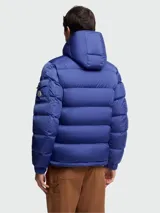 Campera puffer Moncler modelo Maya, color azul, con capucha integrada, cierre frontal bidireccional y bolsillo con solapa en la manga izquierda.