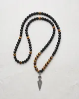 Collar de cuentas esféricas de ónix negro mate y ojo de tigre, con dije central de acero en forma de punta de flecha.