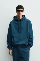 Sudadera con capucha de corte relajado, confeccionada en tejido de algodón con interior perchado. Presenta mangas largas, bolsillo frontal tipo canguro y terminaciones en rib.