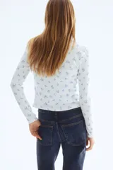 Cardigan ajustado de punto pointelle en color blanco, con pequeño estampado floral azul, escote redondo y cierre frontal de botones con ribetes de picot.