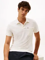 Chomba de manga corta en tejido jacquard elástico color blanco con textura de rayas horizontales. Presenta cuello clásico, tapeta con dos botones y un bolsillo de parche en el pecho con cierre de cremallera y logo bordado.