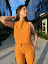 Conjunto de dos piezas color mostaza compuesto por un top sin mangas de cuello redondo y un pantalón de corte recto y tiro alto con cinturón integrado.