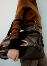 Bolso de hombro tipo hobo, confeccionado en poliuretano con acabado brillante efecto cuero. Presenta un diseño estructurado con correas laterales ajustables mediante hebillas metálicas y un compartimento principal espacioso.