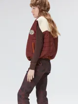 Chaleco de corte cuadrado con diseño bicolor en tonos terracota y crema. Presenta cierre frontal metalizado, parches de nylon en el pecho, interior forrado en corderito y cordón ajustable en el ruedo.