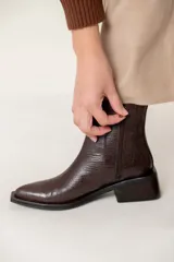 Bota tipo chelsea de caña media con acabado efecto cocodrilo en color chocolate. Presenta paneles elásticos laterales, puntera cuadrada y taco ancho geométrico.