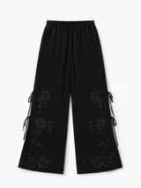 Pantalón negro de corte amplio, con cintura elastizada, bordado floral en la parte inferior y aberturas laterales con tiras para atar.